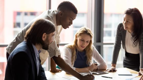 Group of people working together looking at a desk with papers